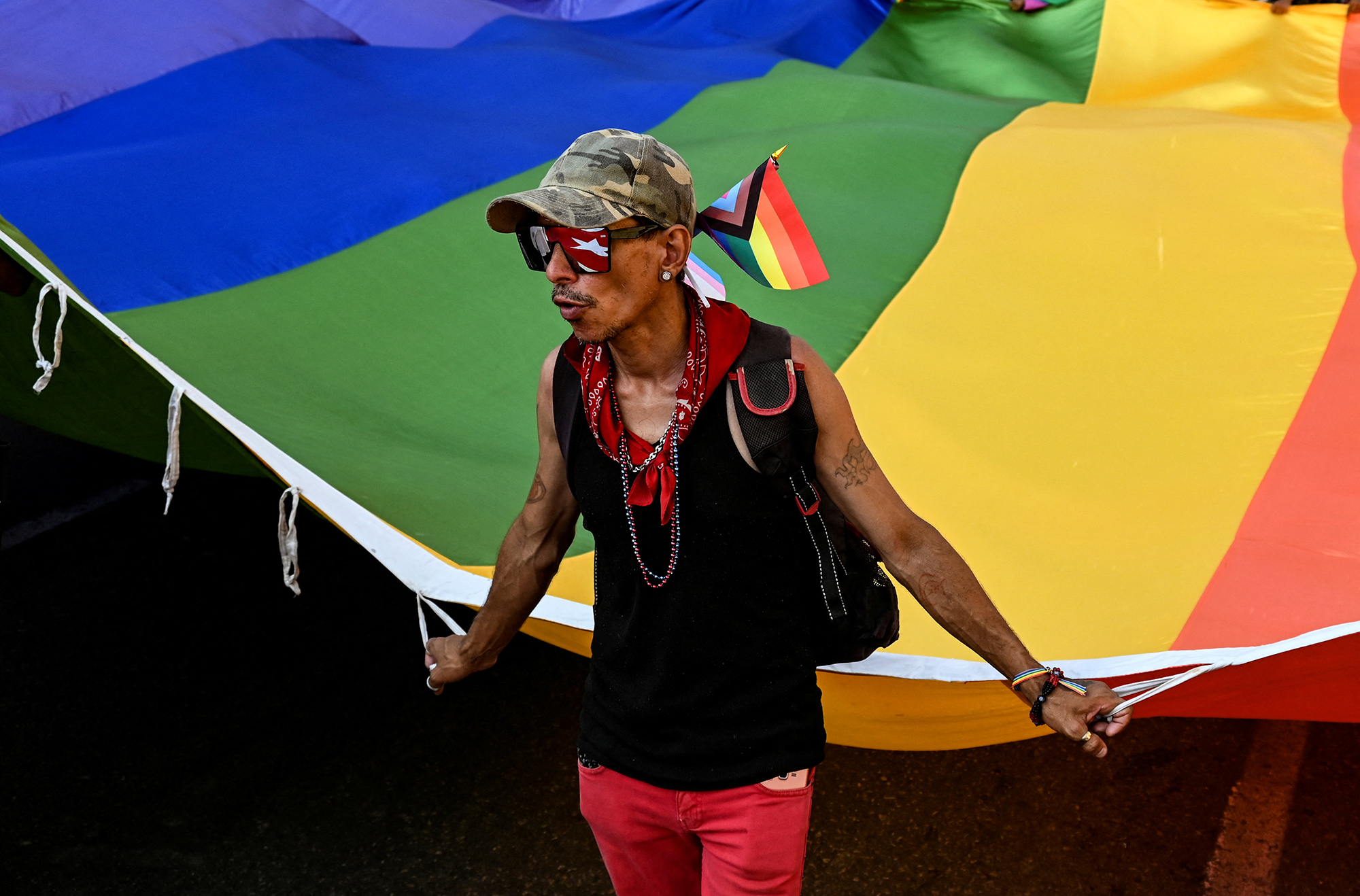 A Cuban man holds a huge rainbow flag 