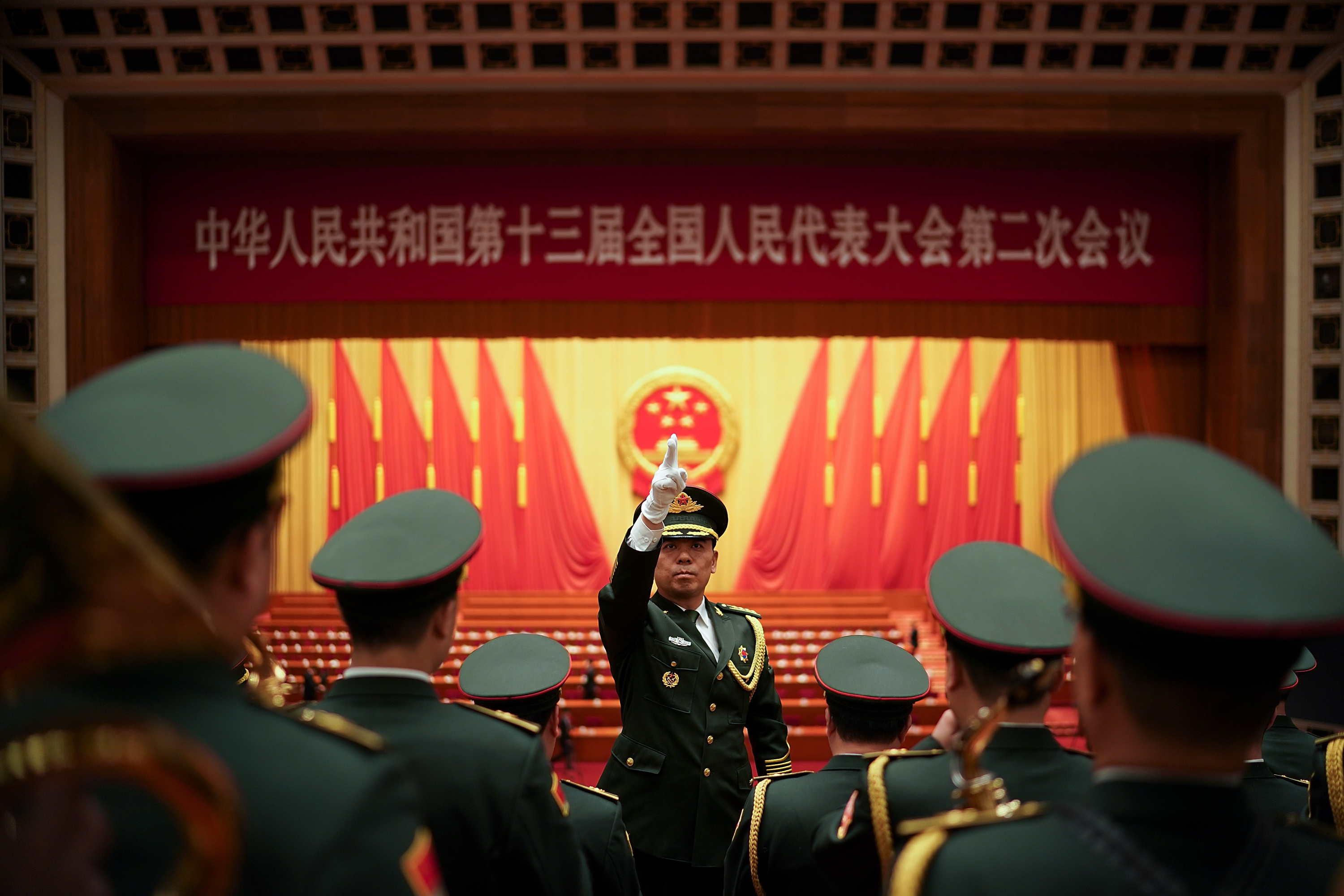 Chinese military officer standing in front of a group of soldiers with Chinese flags in the background.