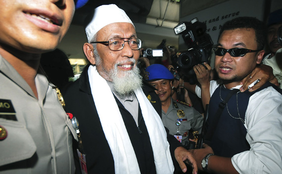 Indonesian Muslim cleric Abu Bakar Bashir is escorted by the police as he arrives at the police headquarters in Jakarta