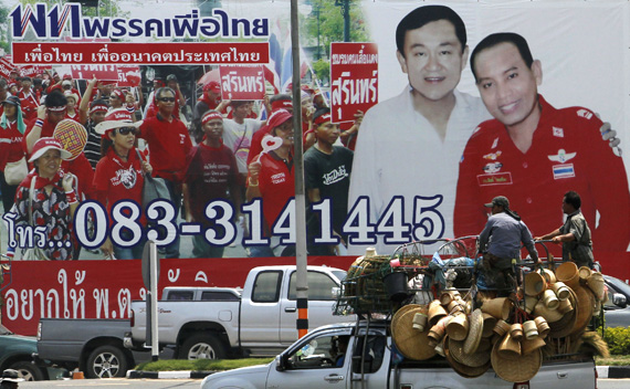 Men atop a truck travel past an election campaign poster showing a candidate for the opposition Puea Thai party posing with ousted former Prime Minister Thaksin Shinawatra in Thailand’s Surin province April 26, 2011.