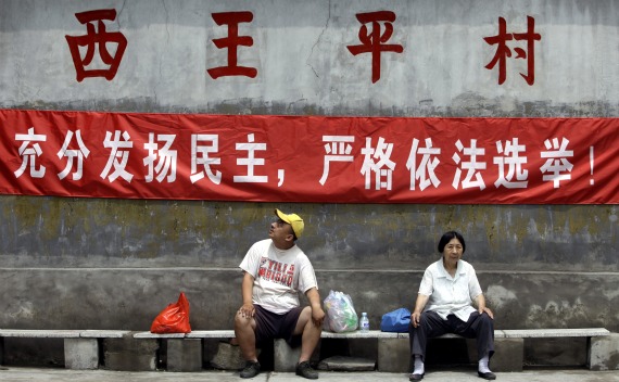 Villagers rest under a campaign banner in the run-up to a democratic election for village committee at Xiwangping Village, in Beijing’s Mentougou District on June 18,2010. The banner reads: “fully develop democracy, strictly elect in accordance to law”