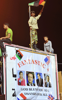 Libyans celebrate near the court house in Benghazi August 23, 2011 after rebel fighters entered Tripoli. The poster below displays images of U.S. Ambassador to the U.N. Susan Rice, British Prime Minister David Cameron, French President Nicolas Sarkozy and U.S. President Barack Obama (L-R). REUTERS/Esam Al-Fetori (LIBYA - Tags: POLITICS)