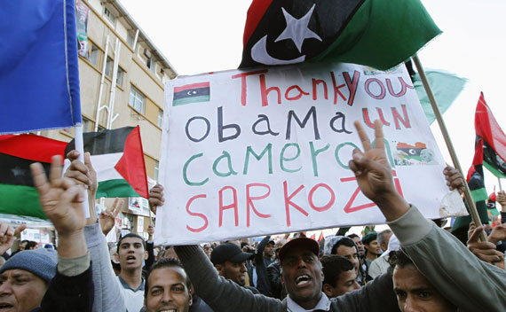 A protester holds a banner beneath a Kingdom of Libya flag during an anti-Gaddafi demonstration in Benghazi on March 31, 2011. 