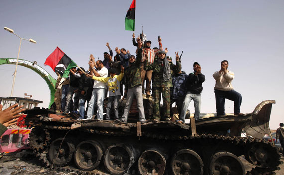 People celebrate atop a destroyed tank belonging to forces loyal to Qaddafi after an air strike by coalition forces in Ajdabiyah.