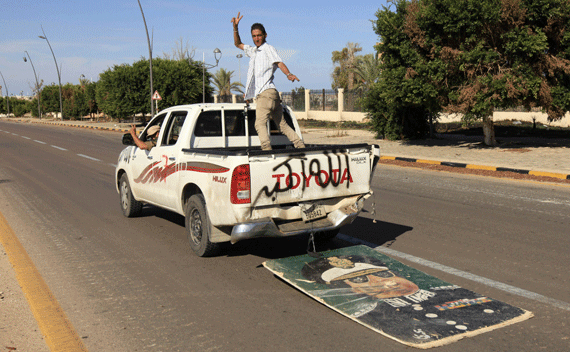 Anti-Gaddafi fighters gesture as they ride in a vehicle, trailed by an image of Muammar Gaddafi, after the fall of Sirte in the town October 20, 2011. Gaddafi was killed on Thursday as Libya’s new leaders declared they had overrun the last bastion of his long rule, sparking wild celebrations that eight months of war may finally be over. Details of the death near Sirte of the fallen strongman were hazy but it was announced by several officials of the National Transitional Council (NTC) and backed up by a photograph of a bloodied face ringed by familiar, Gaddafi-style curly hair. REUTERS/Esam Al-Fetori
