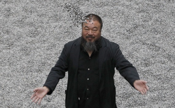 Chinese artist Ai Weiwei throws porcelain sunflower seeds into the air as he poses for a photograph with his installation entitled ’Sunflower Seeds’, at its unveiling at the Tate Modern gallery, in London on October 11, 2010. 