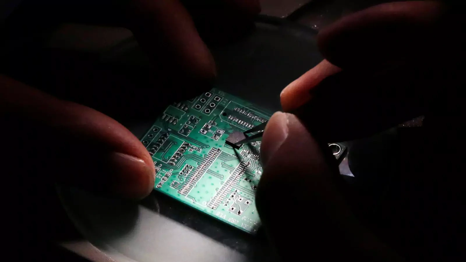 A researcher plants a semiconductor on an interface board, which is placed under a microscope. 
