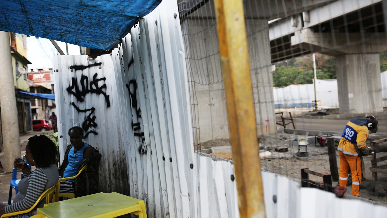 Residents sit behind a divider that separates homes from a bridge of the Transolimpica BRT, an express road built through a shantytown.