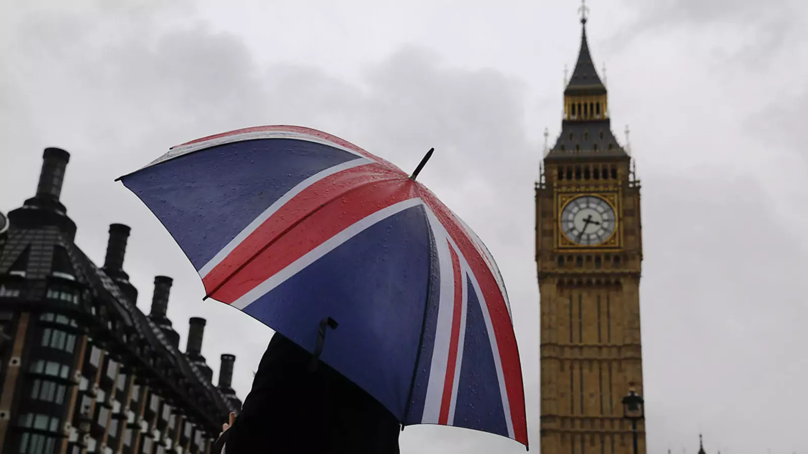 A woman holds a Union flag umbrella in front of the Big Ben clock tower and the Houses of Parliament in London.
