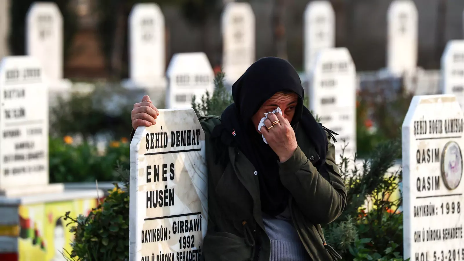 A Syrian Kurdish woman hugs the tombstone of a fallen Syrian Democratic Forces fighter at a cemetery in Qamishli.
