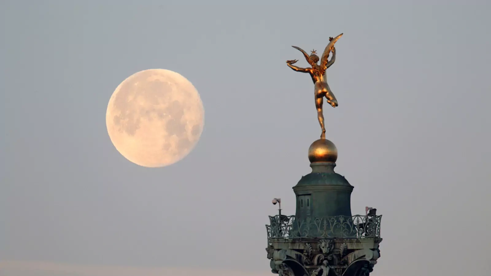 The moon is seen behind the Genie de la Liberte gilded figure on top of the Place de la Bastille’s July Column in Paris.