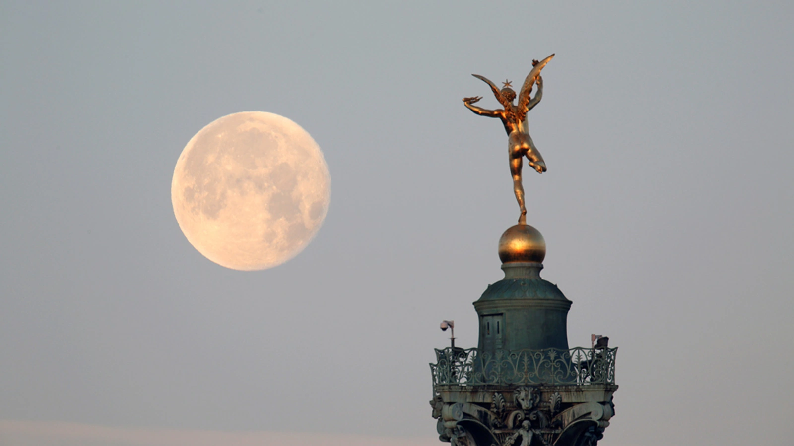 The moon is seen behind the Genie de la Liberte gilded figure on top of the Place de la Bastille’s July Column in Paris.