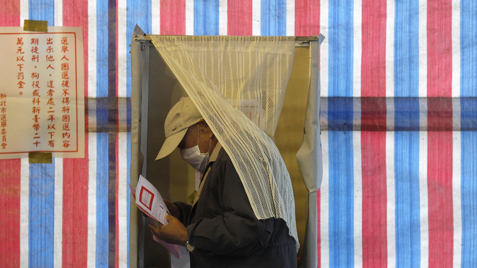 A man wearing a health mask walks out of a voting booth in Xinbei, Taiwan. 
