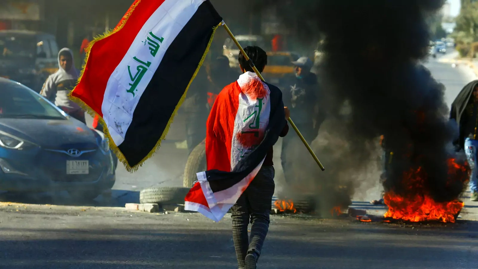 A demonstrator carries an Iraqi flag as he walks near burning tires, during ongoing anti-government protests in Najaf, Iraq January 12, 2020.