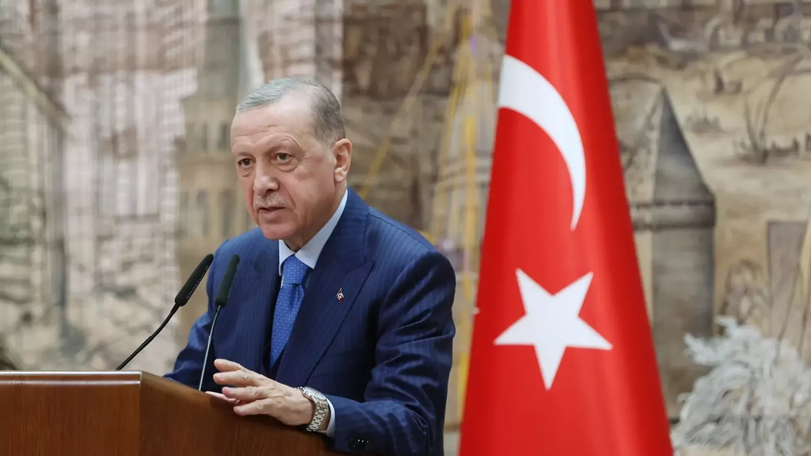 Turkish President, Recep Tayyip Erdoğan in a blue suit speaking at podium