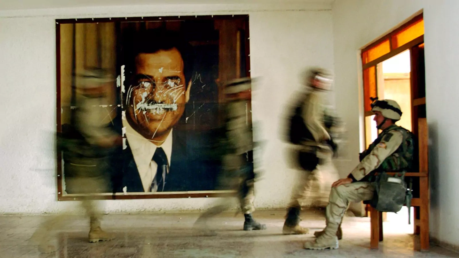 U.S. soldiers walk by a defaced poster of former Iraqi President Saddam Hussein in April 2003.