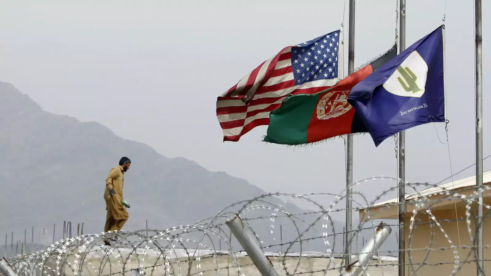 An Afghan working in a U.S military base walks near half mast flags of United States, Afghanistan and Task Force Cacti after a U.S. Army officer was killed by an IED (improvised explosive device) during a patrol in Pesh Valley, at Forward Operating Base J