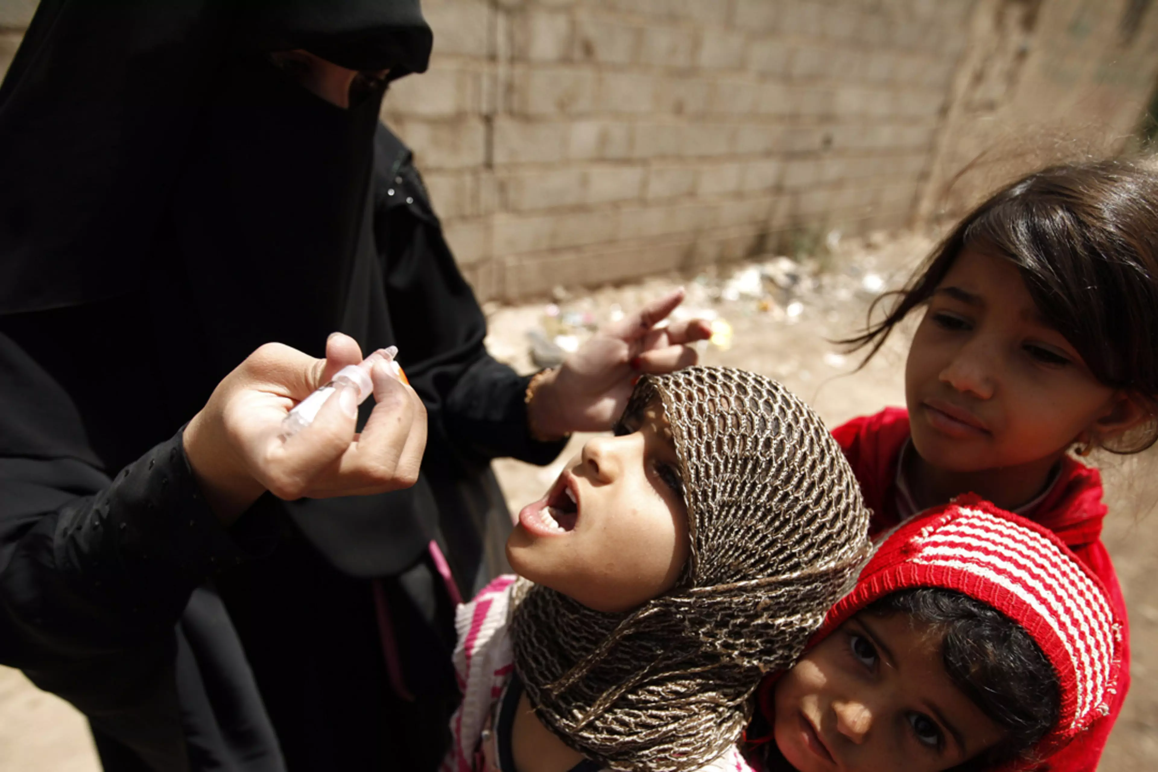 A health worker administers drops of polio vaccine to children in an outskirt of the Yemeni capital Sana'a.