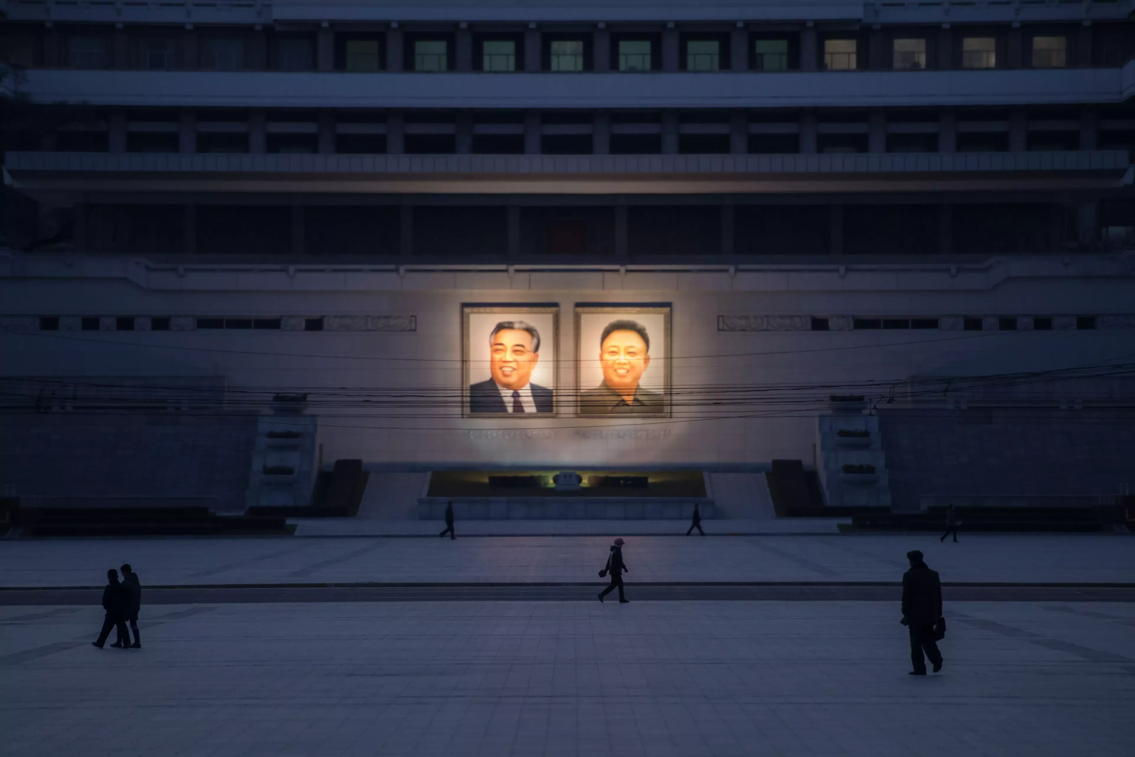 People walk past portraits of Kim Il-sung and Kim Jong-il.