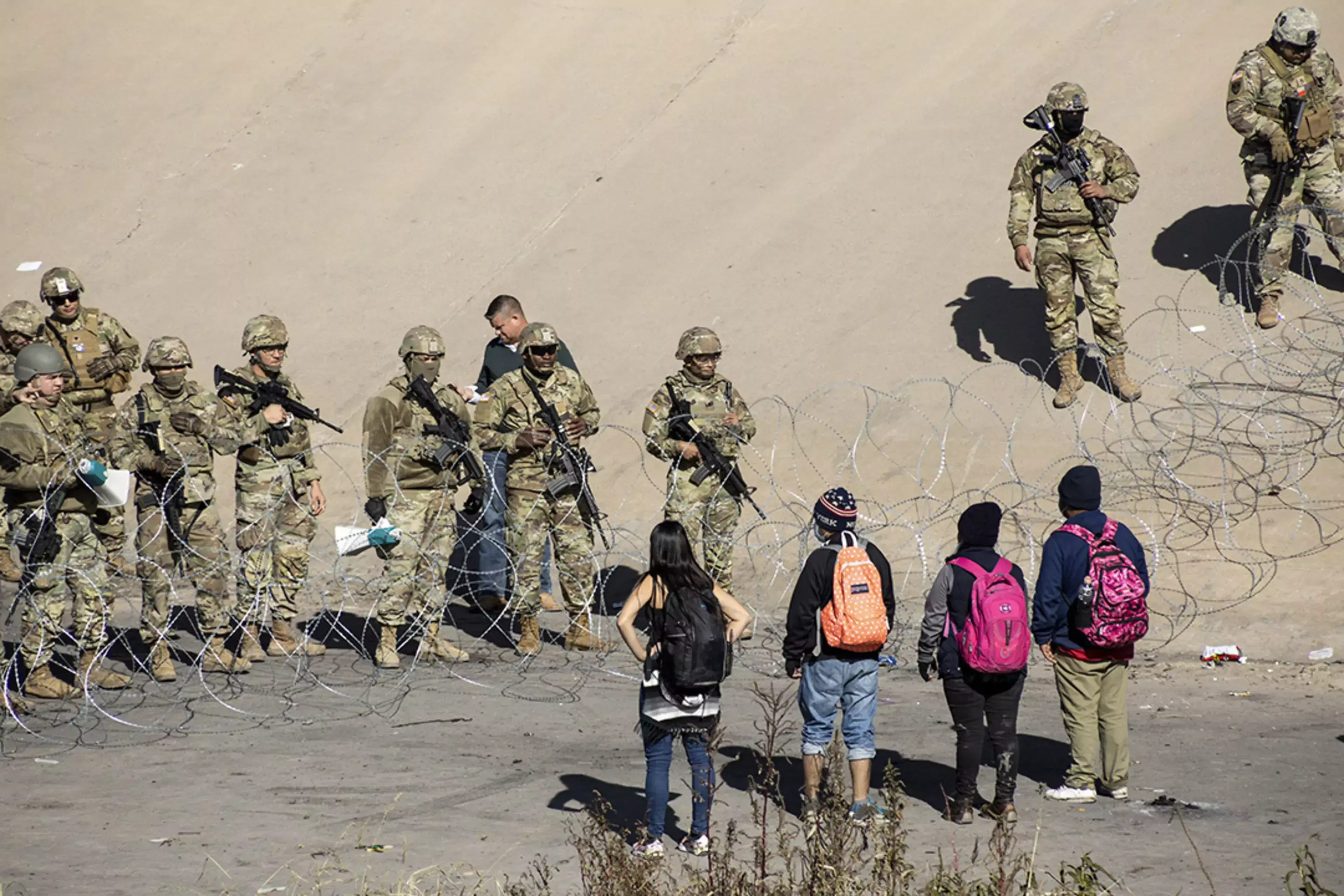Migrants look across the southern U.S. border at Texas National Guard troops.