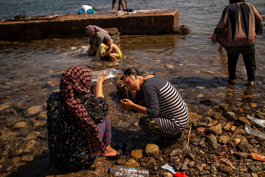 A migrant pours water on the head of another one on the beach near Mytilene, on the Greek island of Lesbos