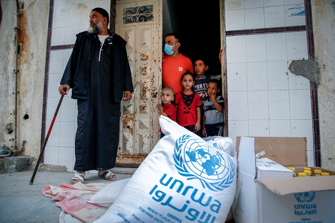 Members of a Palestinian family, some clad in mask due to the COVID-19 coronavirus pandemic, stand through the door of their home as they receive food aid provided by the United Nations Relief and Works Agency for Palestine Refugees (UNRWA) in Gaza City