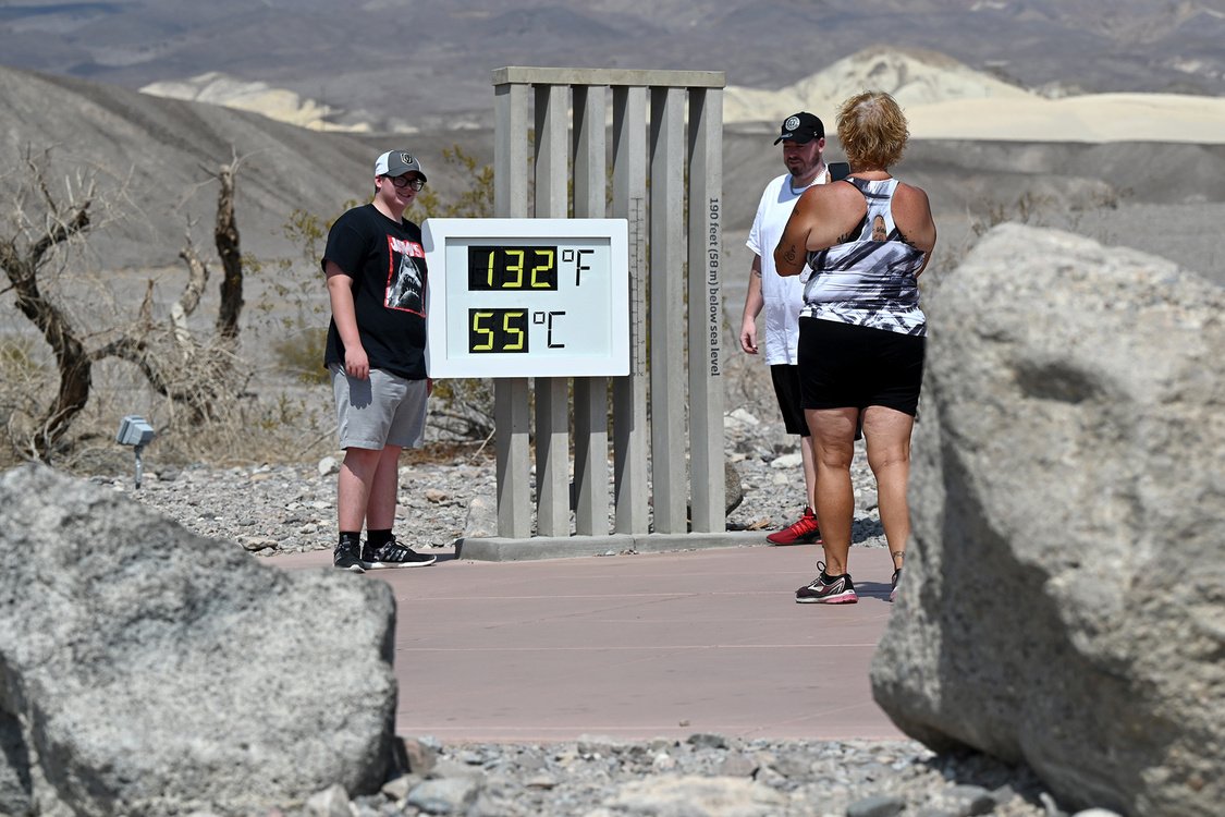 People pose by an unofficial thermometer reading 132 degrees Fahrenheit in Death Valley