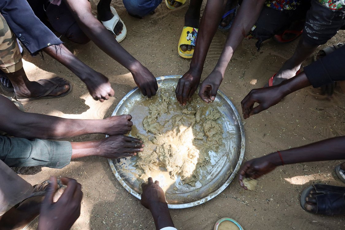 Hands of refugees are seen getting food from a single platter, in the Adre Sudanese refugee camp in Adre, Chad..