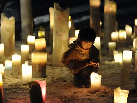 Child looks at candle flame during event to pray for reconstruction of areas devastated by March 2011 quake and tsunami, in Iwanuma.