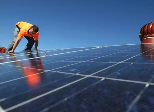A solar system installer adjusts new solar panels on the roof of a house (Tim Wimborne/Courtesy Reuters).