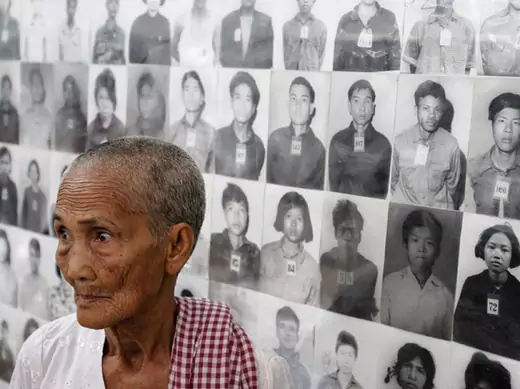 A survivor of the Khmer Rouge regime Hem Sakou stands in front of portraits of victims at the Tuol Sleng (S-21) genocide museum in Phnom Penh