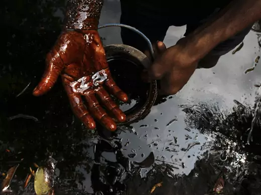 A man samples crude oil at the bank of a polluted river in Bidere community in Ogoniland in Nigeria's delta region