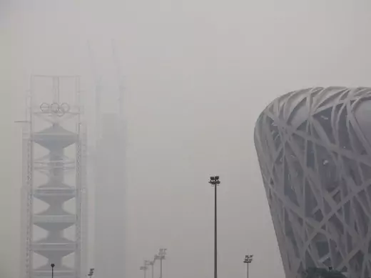 The National Stadium, also known as the 'Bird's Nest', can be seen next to a tower bearing the Olympic rings and a building under construction on a high air pollution day in Beijing on June 6, 2012.
