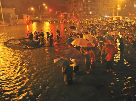 Rescuers and residents stand next to a stranded car which is being pulled up from a flooded street under the Guangqumen overpass amid heavy rainfalls in Beijing on July 21, 2012.