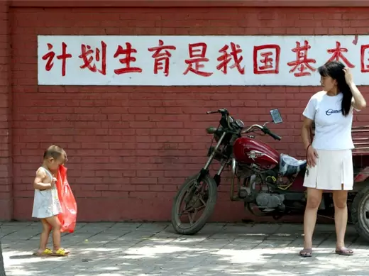 A young Chinese mother watches her child in front of a sign reading "birth control is a basic state policy of our country" in Beijing on July 23, 2002.