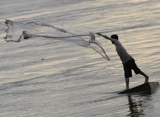 A man casts a fishing net on the banks of the Mekong river.