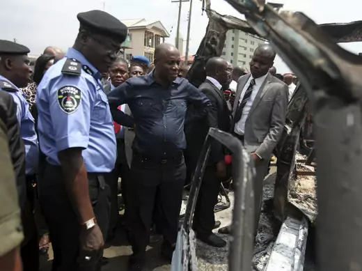 Nigerian River state governor Amechi stands with security officials to assess a burnt commercial bus (Akintunde Akinleye/Courtesy Reuters).