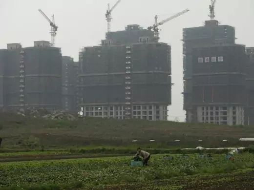 A farmer works in her field in front of a residential construction site in Shanghai on April 25, 2012. 