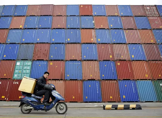 A man rides his motorcycle past shipping containers at the Port of Shanghai (Aly Song/Courtesy Reuters).