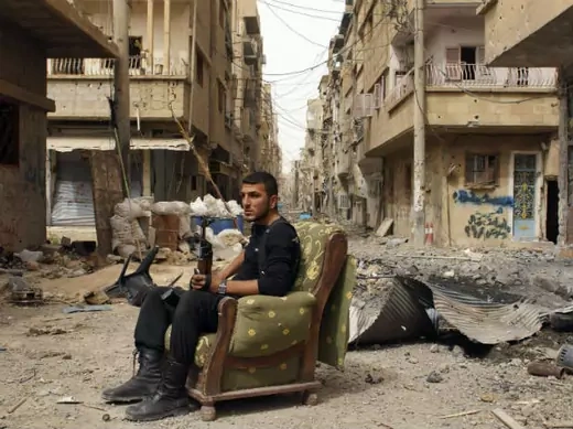 A member of the Free Syrian Army holds his weapon as he sits on a sofa in the middle of a street in Deir al-Zor April 2, 2013 (Ashawi/Courtesy Reuters). 