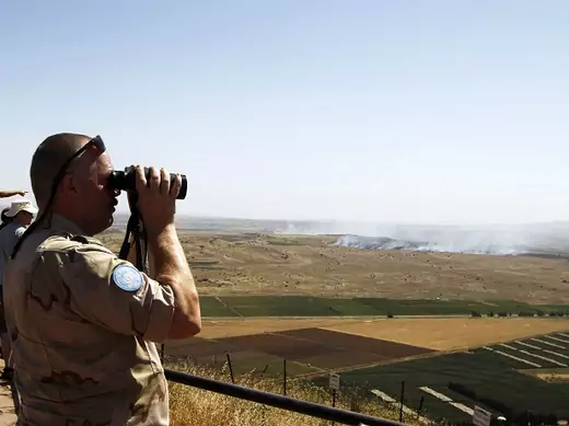 A U.N. peacekeeping soldier uses binoculars to watch fighting between forces loyal to Syrian regime and rebels opposed to Syrian President Assad, from Israeli-occupied Golan Heights