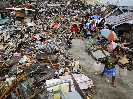 A survivor carries water cans as he searches for fresh water in an area devastated by Typhoon Haiyan in Tacloban