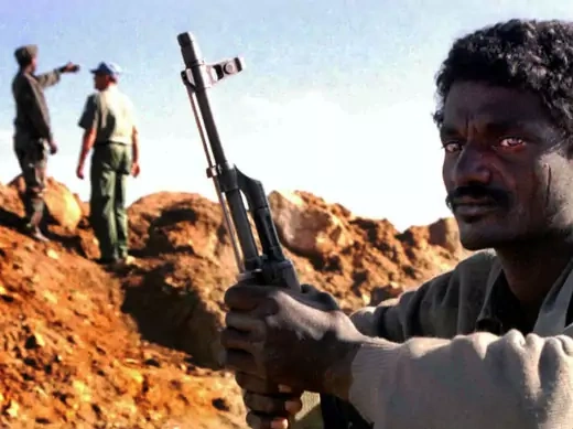 An Eritrean soldier sits on guard duty as a UN military observer and his Eritrean counterpart inspect a frontline trench near the Eritrean town of Senafe on October 20, 2000.