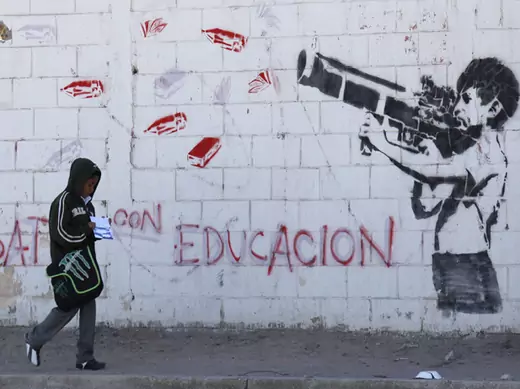 A boy walks past a mural depicting a child shooting an RPG loaded with school supplies in Ciudad Juarez