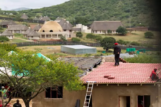 A member of the Economic Freedom Fighters (EFF) stands on the roof of a house they built for an elderly woman, near the homestead of South African President Jacob Zuma (in the background), in Nkandla January 11, 2014.