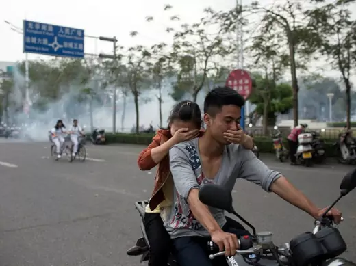 Residents cover their faces as they ride a motorcycle along a street after tear gas was released by police to disperse a protest against a chemical plant project in Maoming, Guandong province, China on March 31, 2014. (Stringer/Courtesy Reuters)