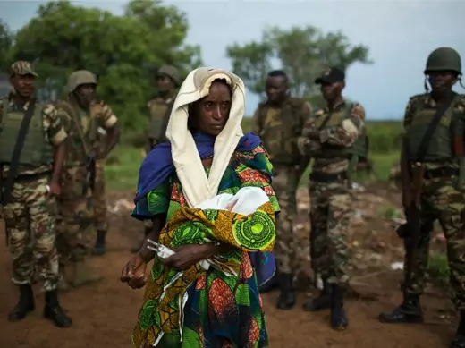 A woman holding a newborn stands in front of African Union troops in the Central African Republic, April 2014 (Courtesy Reuters/Siegfried Modola). 