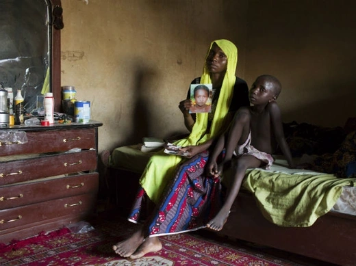 Rachel Daniel, 35, holds up a picture of her abducted daughter Rose Daniel, 17, as her son Bukar, 7, sits beside her at her home in Maiduguri, May 21, 2014. (Joe Penney/Courtesy Reuters)