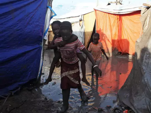 A South Sudanese girl displaced by the conflict carries a younger boy on her back as they walk through mud in a flooded camp for internally displaced people at the UNMISS base in Malakal, Upper Nile State, May 30, 2014.   (Andreea Campeanu/Courtesy Reuters)