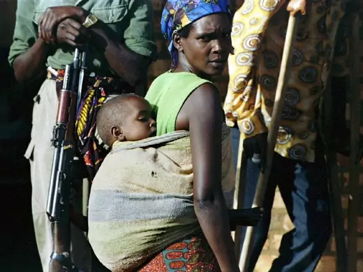 A Tutsi woman passes between a guerilla from the Rwandan Patriotic Front on the left and a wounded man on the right, Rwanda, May 1994 (Courtesy Reuters).